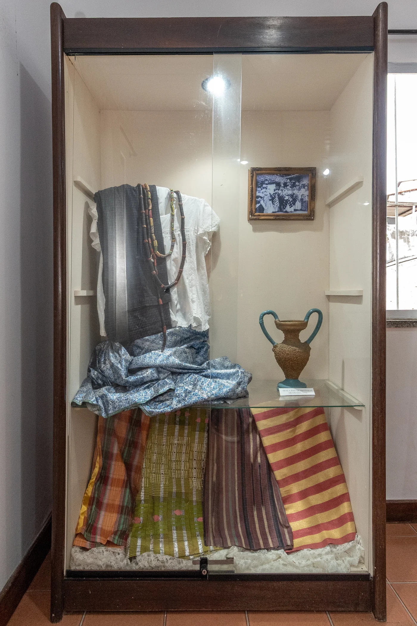 Indumentária religiosa composta de Saia em cetim, Camisa de Crioula em richelieu, Bata de Cambraia bordada e bico, Alaká (Pano da Costa) e Laguidbás com monjolos, búzios, coral e murano / Alakás (Panos da Costa) / Foto da Cerimônia das Quartinhas de Oxossi de1902 e Quartinha dessa cerimônia